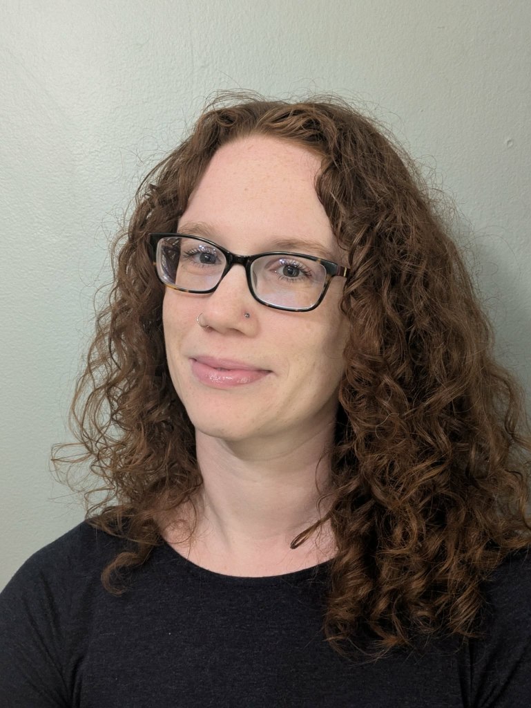 Headshot of a woman with red hair and glasses.